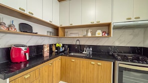 A kitchen with wooden cabinets, a black countertop, a red coffee maker, a sink, and a stove. - SHB Condomínio com 5 Quartos e Lazer (Guarujá)