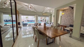 Ampla sala de estar com uma grande mesa de jantar de madeira, assentos confortáveis e vista para uma piscina ao ar livre.