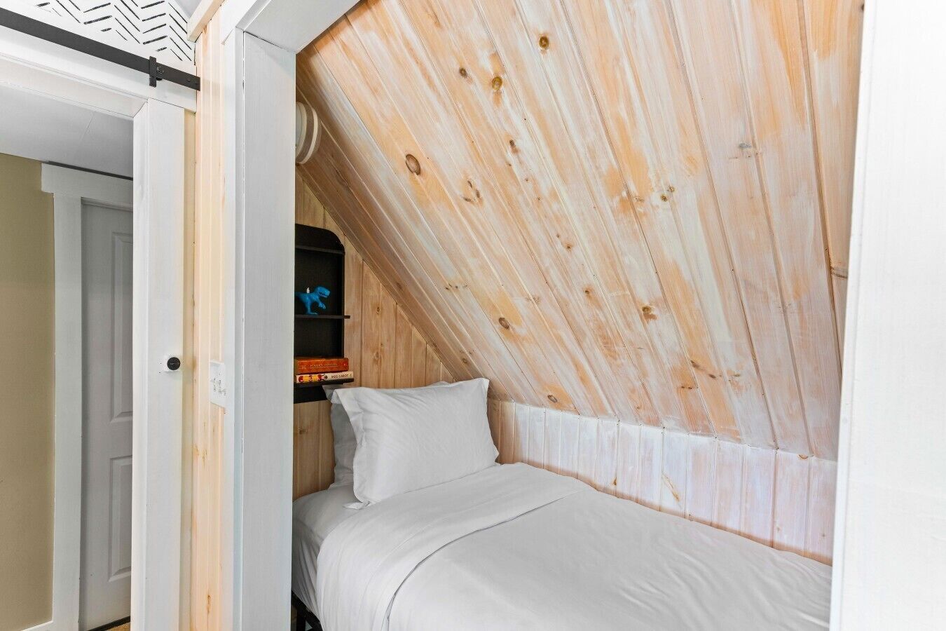 A bedroom with a sloped ceiling, a bed, and a shelf with books and a toy.