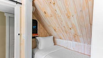 A bedroom with a sloped ceiling, a bed, and a shelf with books and a toy.