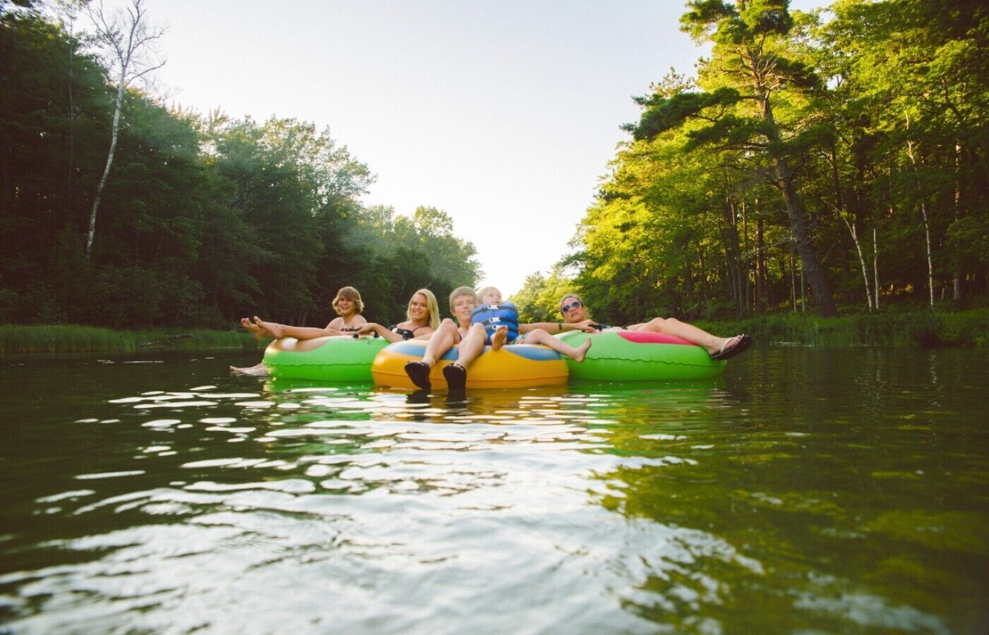 A group of people on inflatable tubes in a body of water surrounded by trees.