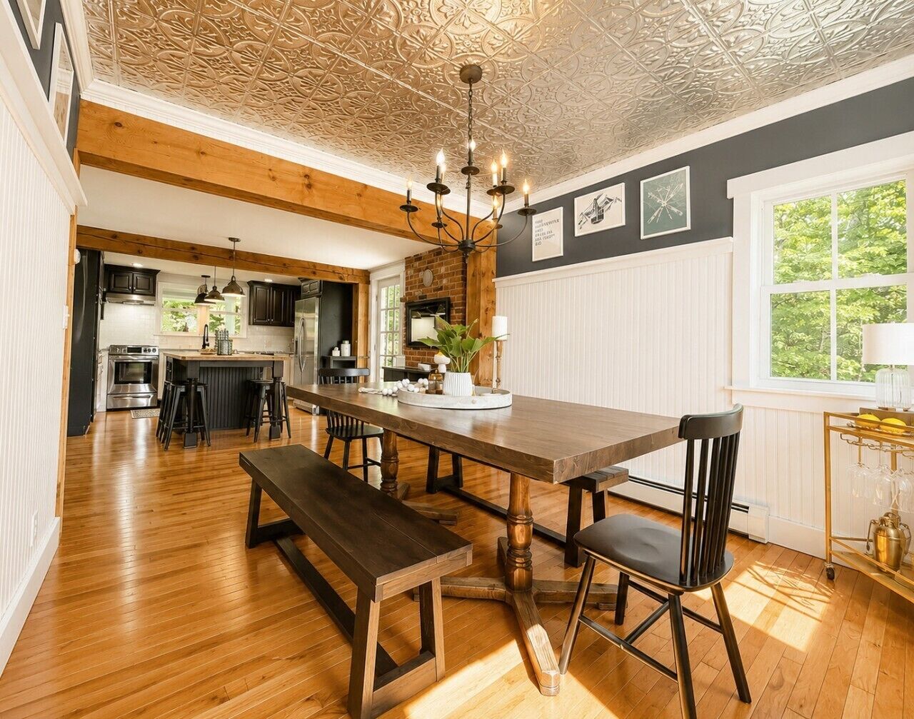 A spacious dining area with a wooden table and benches, a kitchen in the background, and a decorative ceiling.