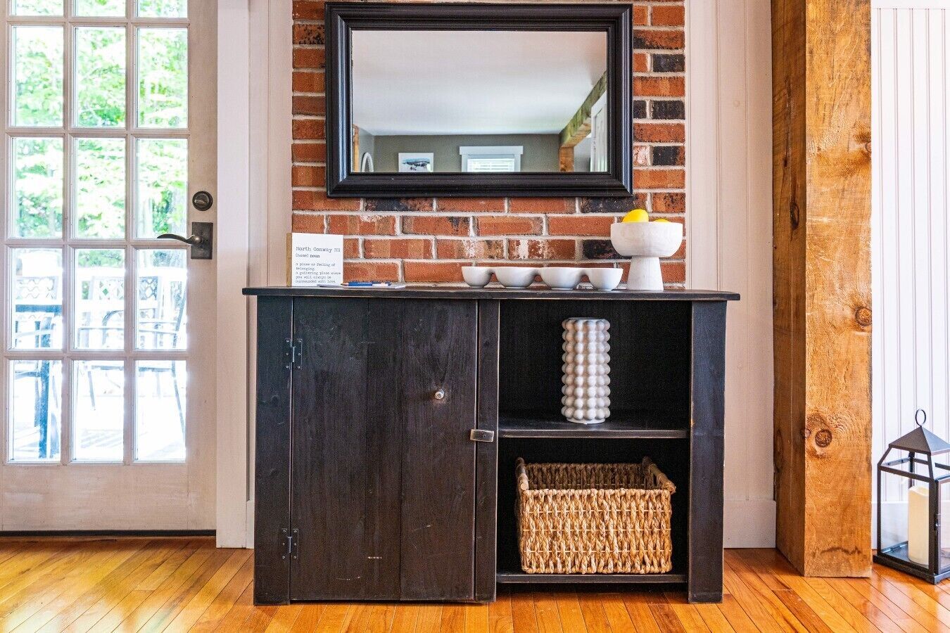 A dark wooden cabinet with a mirror above it, a wicker basket, and a white vase on the top shelf.