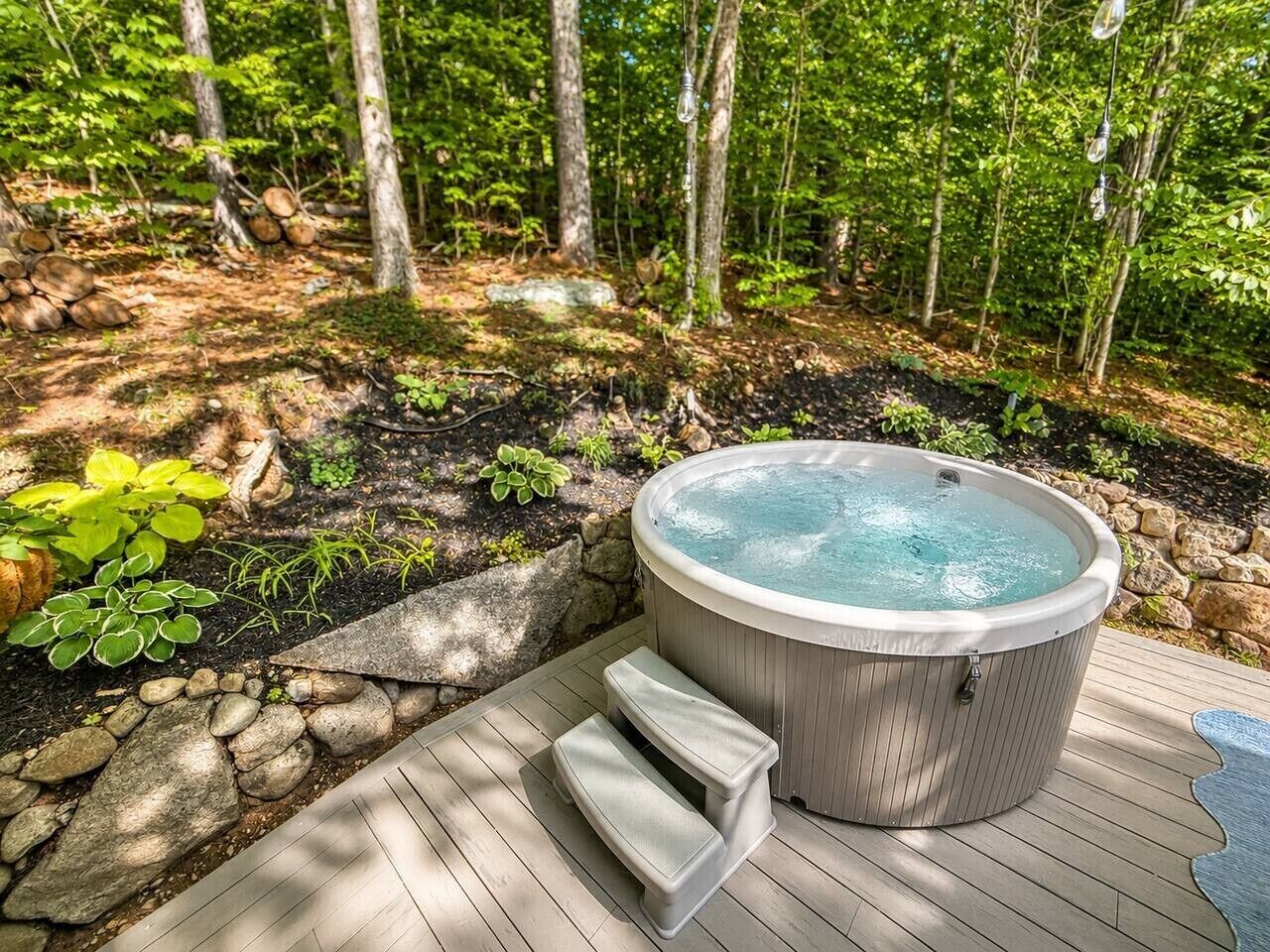 A hot tub in a forested area with a wooden deck and steps leading to it.