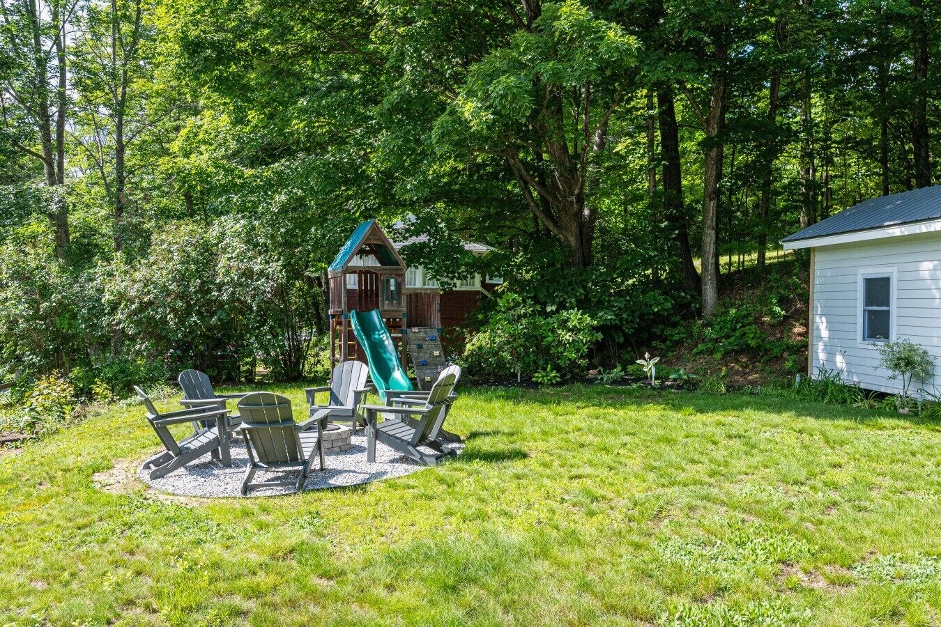 Un jardin avec une cabane en bois, un toboggan et un espace détente comprenant des chaises et une table.