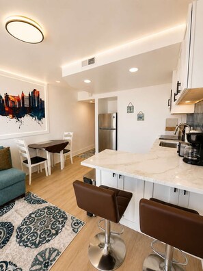 Een moderne keuken met een marmeren aanrecht, roestvrijstalen apparatuur en een kunstwerk van een stadsgezicht.