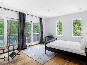 Ein Schlafzimmer mit Bett, Schreibtisch, Stuhl und großen Fenstern mit Vorhängen.