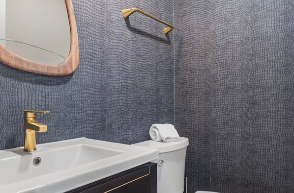 Un baño con lavamanos blanco, grifo dorado y una toalla en la pared.