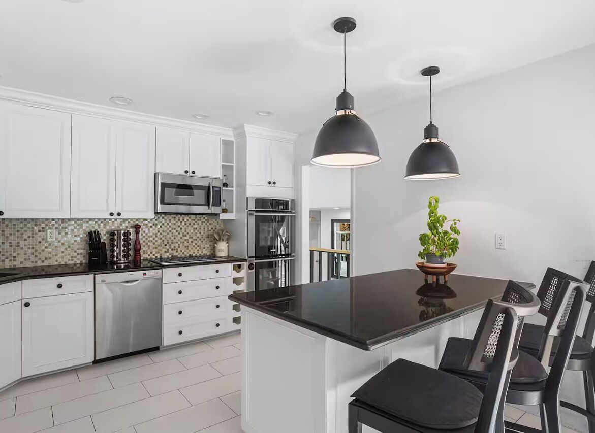 Una cocina moderna con armarios blancos, electrodomésticos de acero inoxidable y una isla central con encimera negra.