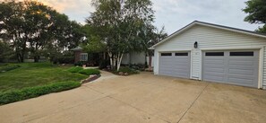 A residential driveway leading to a garage with two doors, surrounded by a well-maintained lawn and trees.