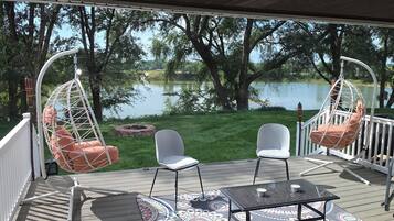 A deck with two hanging chairs, a table, and chairs facing a lake.