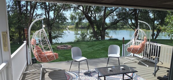 A deck with two hanging chairs, a table, and chairs facing a lake.