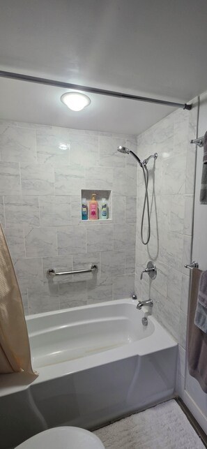 A modern bathroom with a bathtub, shower, and a shelf with toiletries.
