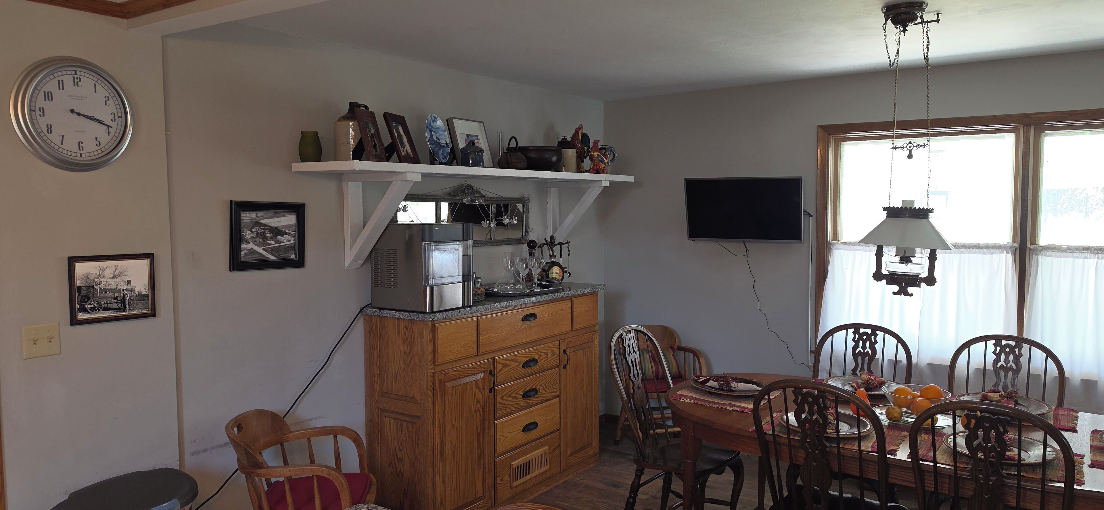 A kitchen with a refrigerator, wooden cabinets, a dining table with chairs, and a wall-mounted clock.