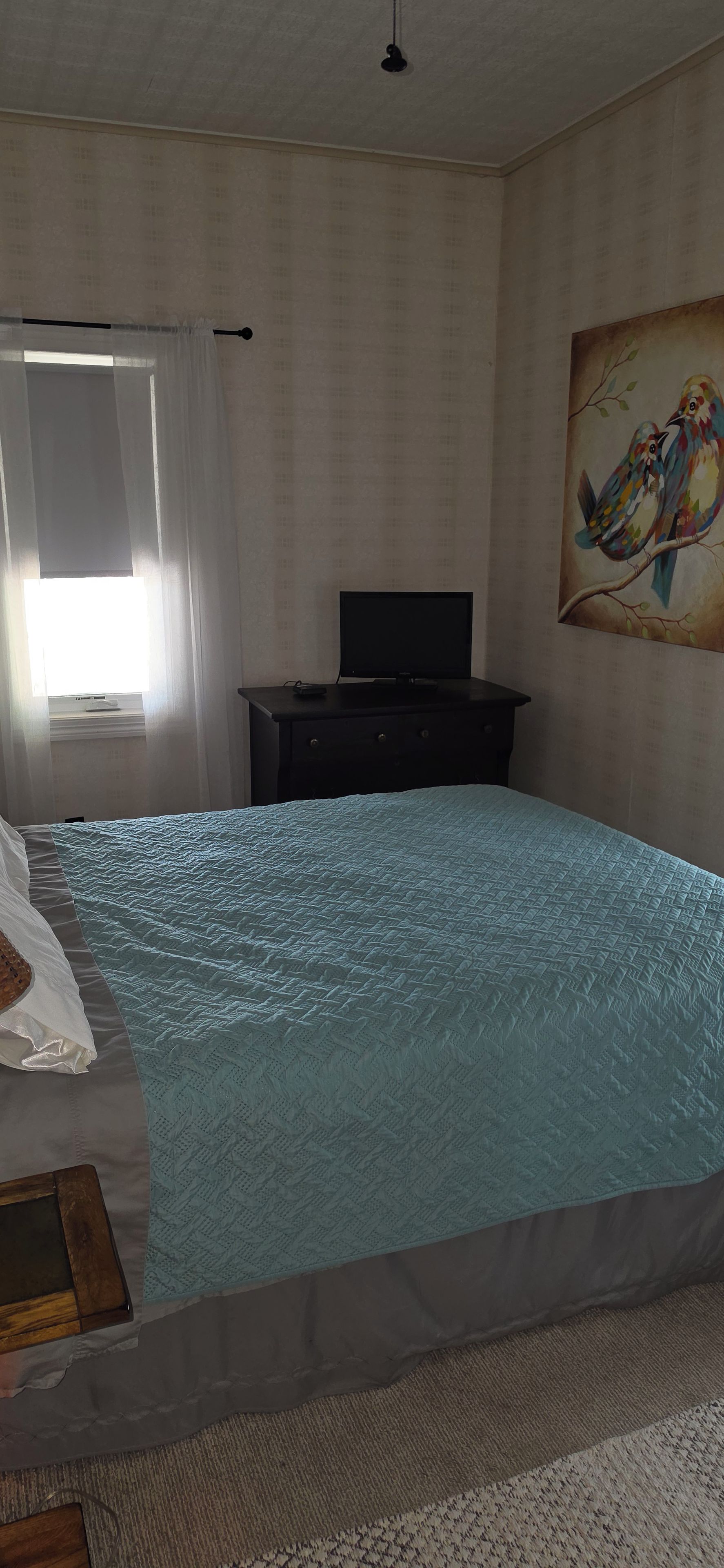 A bedroom with a bed, a desk, a chair, a painting, and a window with curtains.