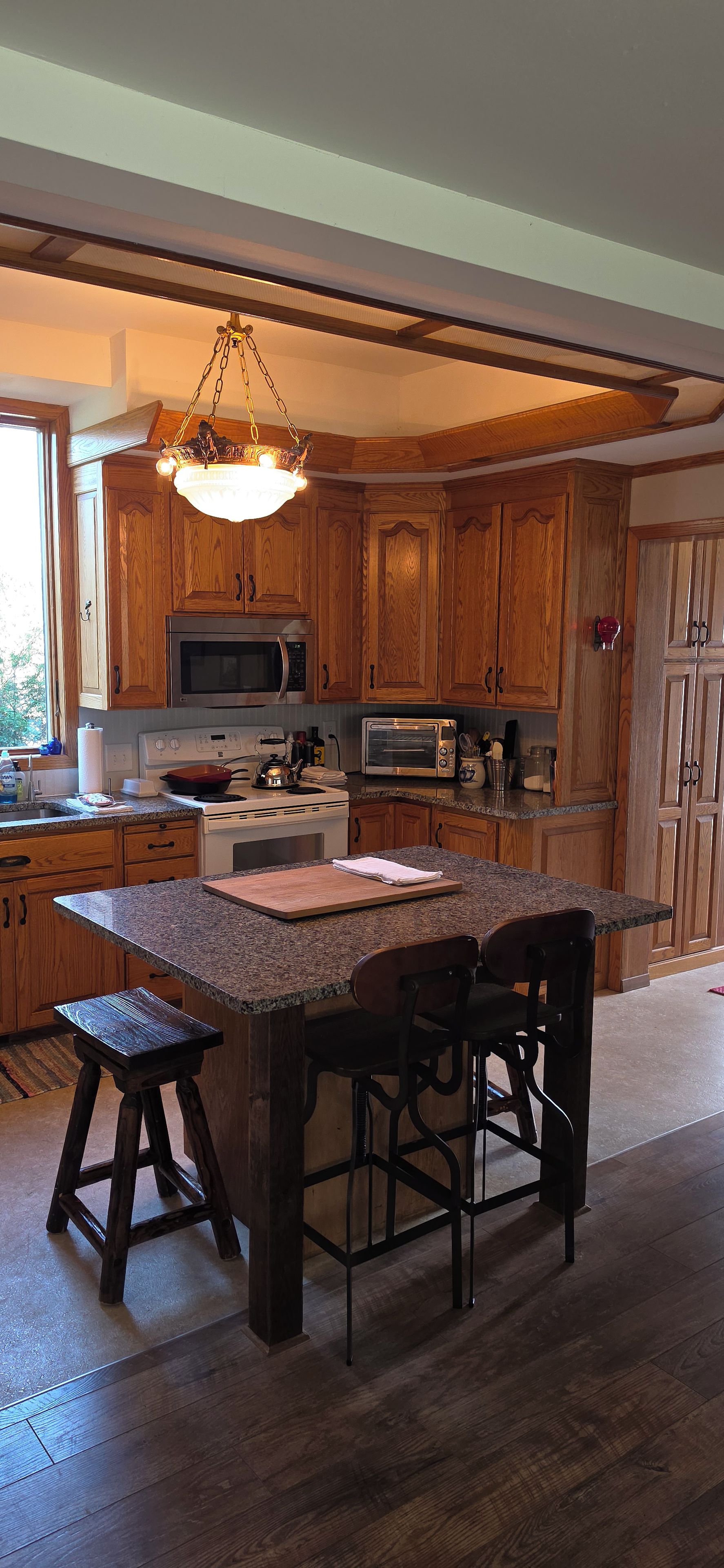 A kitchen with wooden cabinets, a granite countertop, a central island with stools, and a hanging light fixture.