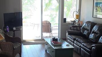 A living room with a sofa, a coffee table, a television, and a window with a view of greenery.