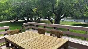 A wooden deck with a table and chairs, surrounded by trees and a view of a body of water.