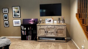 A living room with a flat-screen TV mounted on the wall, a wooden cabinet with decorative items, and a bookshelf filled with books.
