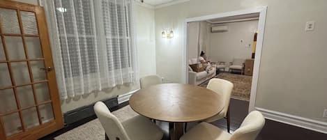 A dining area with a round table and four chairs, a wooden door with glass panels, and a living room in the background.