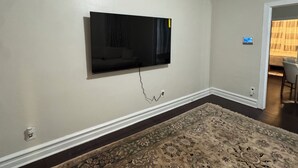 A room with a mounted flat-screen TV, a patterned carpet, and a door leading to another room. - Spacious Brooklyn 4BR/2BA Across 2 Private Floors with Yard (Brooklyn)