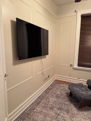 A room with a mounted flat-screen TV, a patterned carpet, a window with blinds, and a door with a glass panel.