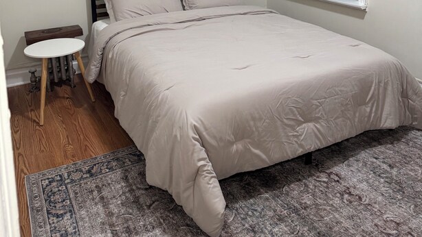 A bedroom with a bed, a small round table, a window with blinds, and a patterned rug. - Spacious Brooklyn 4BR/2BA Across 2 Private Floors with Yard (Brooklyn)