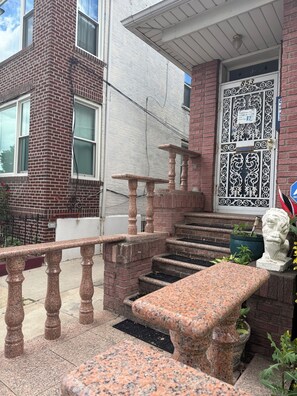 Ein Backsteinhaus mit einem Metallgitter, einer Steinsitzbank und einer Statue.
