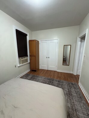 Un dormitorio con cama, armario, espejo y ventana con persianas.