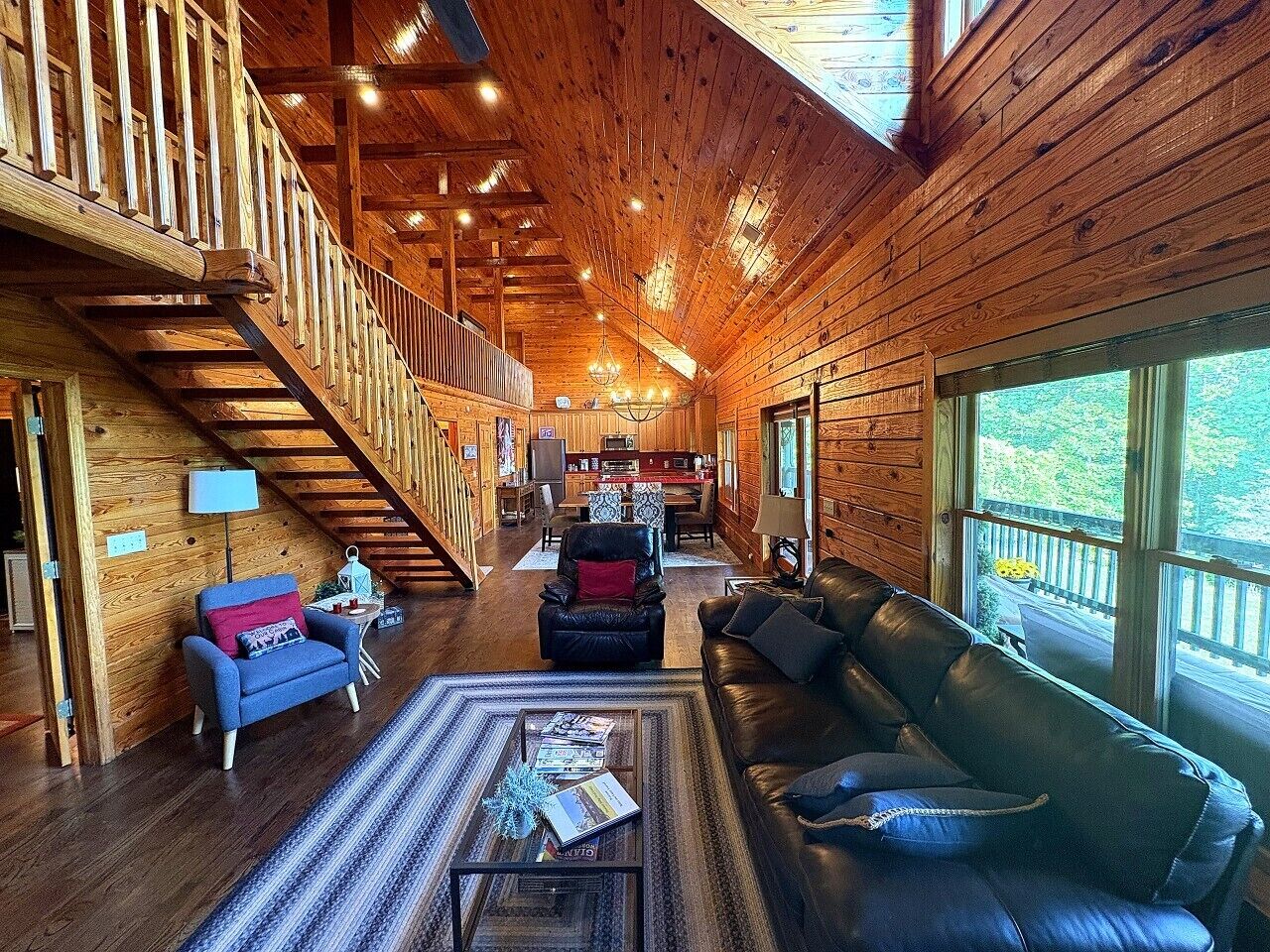 Ein geräumiger Holzinnenraum mit einer Treppe, einem Wohnbereich mit Sofa und Sesseln und großen Fenstern mit Blick ins Freie.
