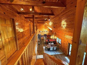 A wooden cabin interior with a dining area, kitchen, and a staircase leading to an upper level.