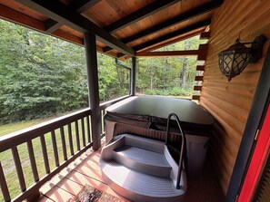 A covered outdoor seating area with a bench and a table, surrounded by a wooden deck and a railing.