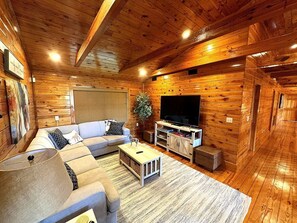 Ein gemütliches Blockhaus-Interieur mit einem Ecksofa, einem Flachbildfernseher und einer Holzbalkendecke.
