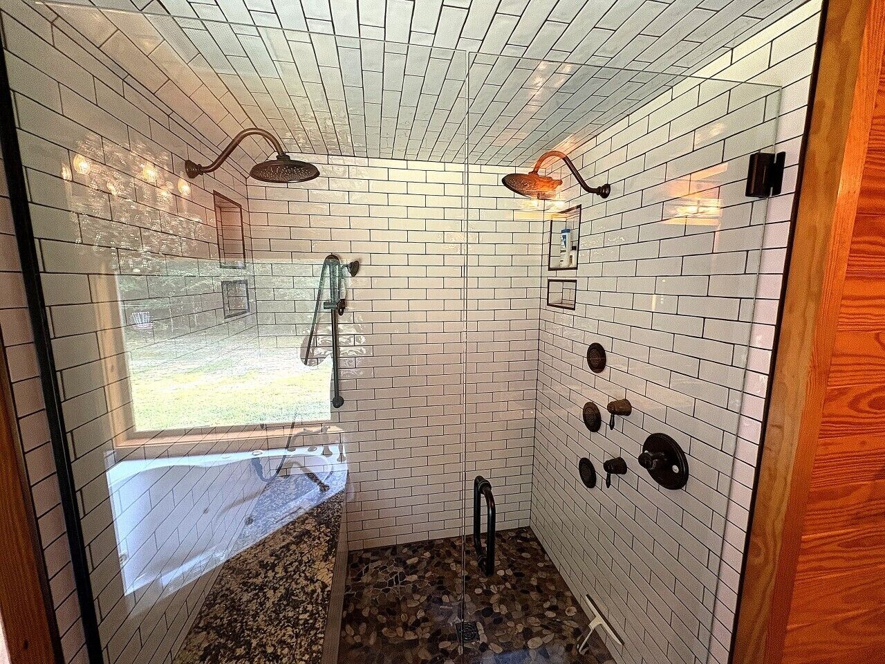 A bathroom with white tiled walls, a shower area, and a window providing a view of the outdoors.