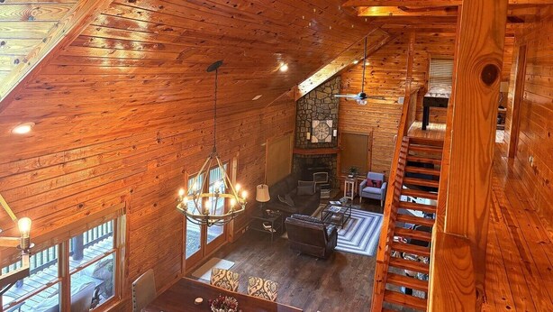A wooden interior with a fireplace, seating area, and a staircase. - Authentic Log Cabin • Hot Tub, Game Room & Yard Games • Sleeps 12 • Wine Country (Mount Airy)
