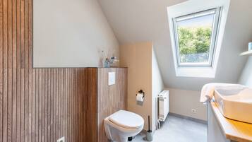 A modern bathroom with a wooden panel wall, a toilet, a radiator, and a window providing natural light.