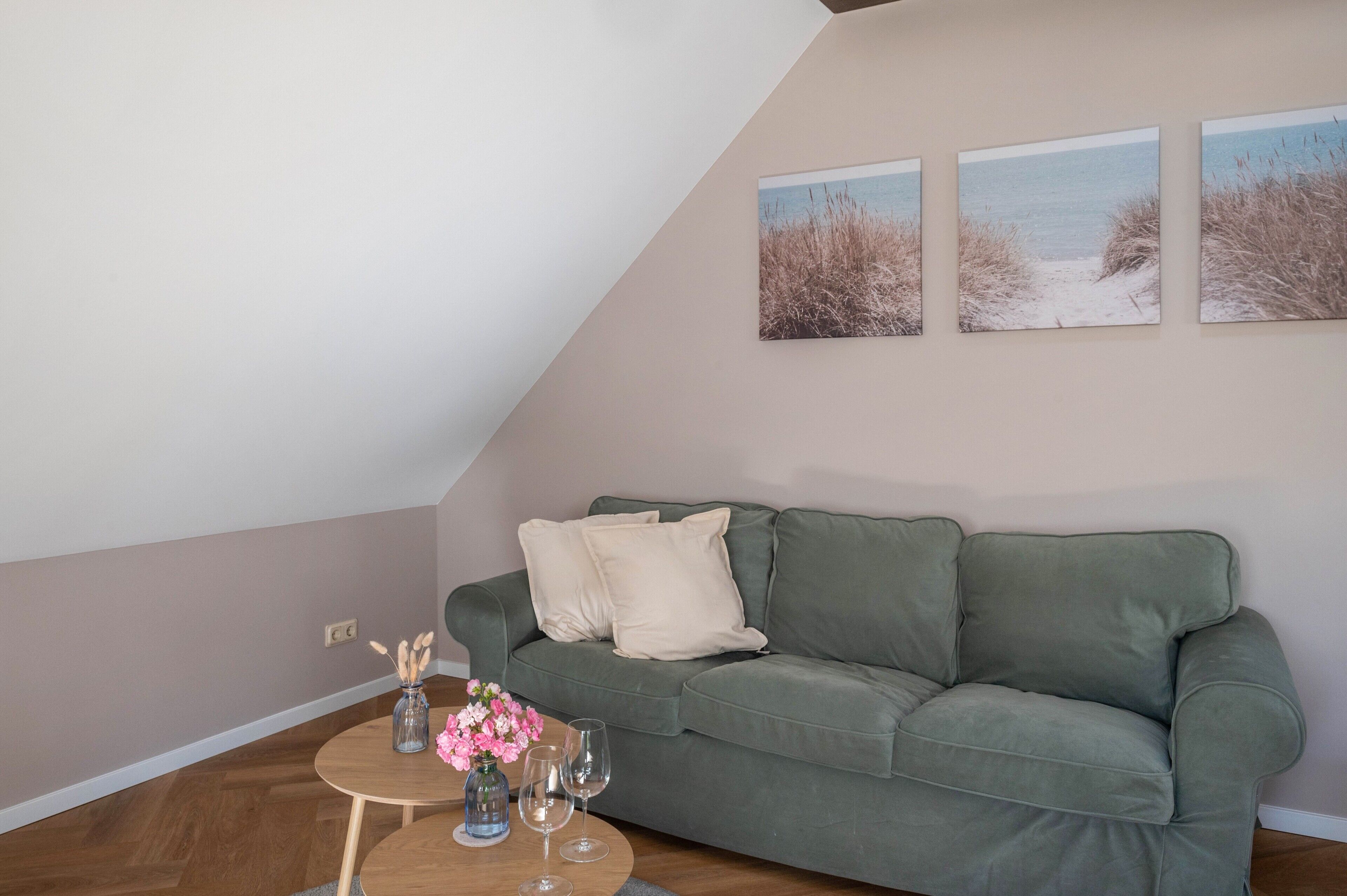 En stue med en grøn sofa, et rundt bord med en vase blomster og tre billeder i rammer på væggen.