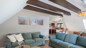 A living room with two green sofas, a wooden coffee table, and a kitchen in the background.
