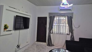 A living room with a TV, a door, a window with curtains, and a ceiling fan. - 2-bedroom serviced apartment in serene Benin City with AC comfort (Benin City)