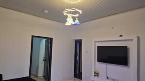 A modern living room with a flat-screen TV mounted on the wall, a round coffee table, and a ceiling light fixture. - 2-bedroom serviced apartment in serene Benin City with AC comfort (Benin City)