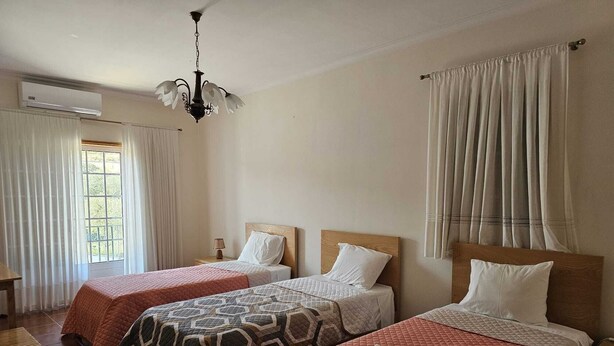A hotel room with two beds, a chandelier, an air conditioning unit, and a window with curtains.
