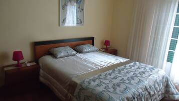 Una cama bien hecha con una colcha estampada, dos almohadas y un cabecero. Se ven dos mesitas de noche con lámparas y un cuadro colgado en la pared.
