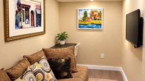 Ein Wohnzimmer mit einer Couch, einem flachbildfernseher an der Wand und zwei gerahmten Kunstwerken.
