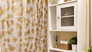 Une salle de bain comprenant des toilettes, un rideau de douche orné de motifs de feuilles, un lavabo et un miroir.
