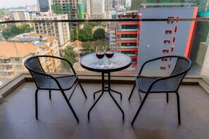 Ein Balkon mit zwei Stühlen und einem Tisch, ein Glas Rotwein und Blick auf die Stadt.
