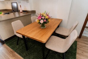 Ein Essbereich mit einem Holztisch, vier Stühlen, einer Blumenvase, einer Küchenzeile und einem grünen Teppich.
