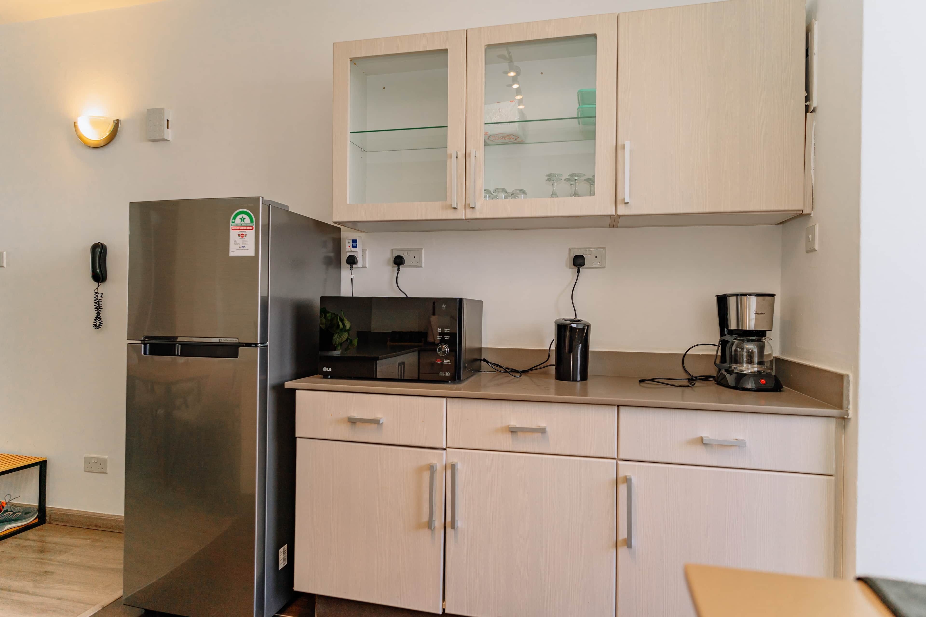 A compact kitchen with a refrigerator, microwave, coffee maker, and cabinets.