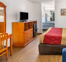 Habitación de hotel con tocador de madera, televisor, cama con colcha roja y beige, y una silla.