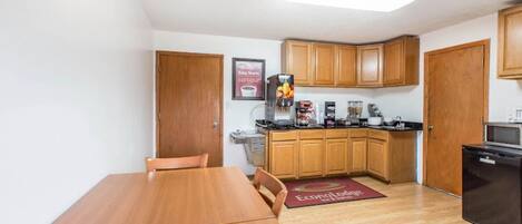 Cocina pequeña con gabinetes de madera, cafetera y refrigerador.