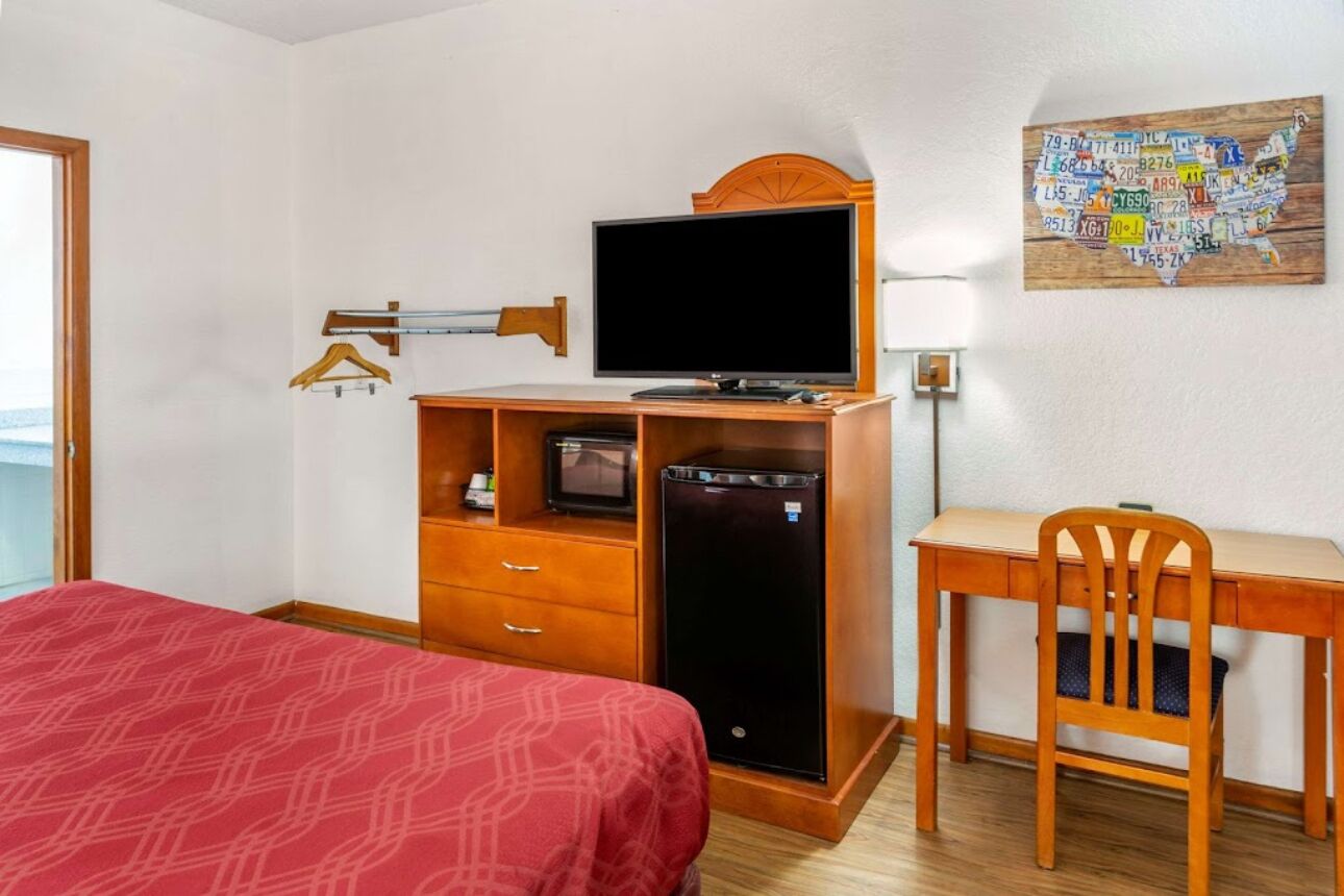 A hotel room with a bed, a desk, a television, and a refrigerator.